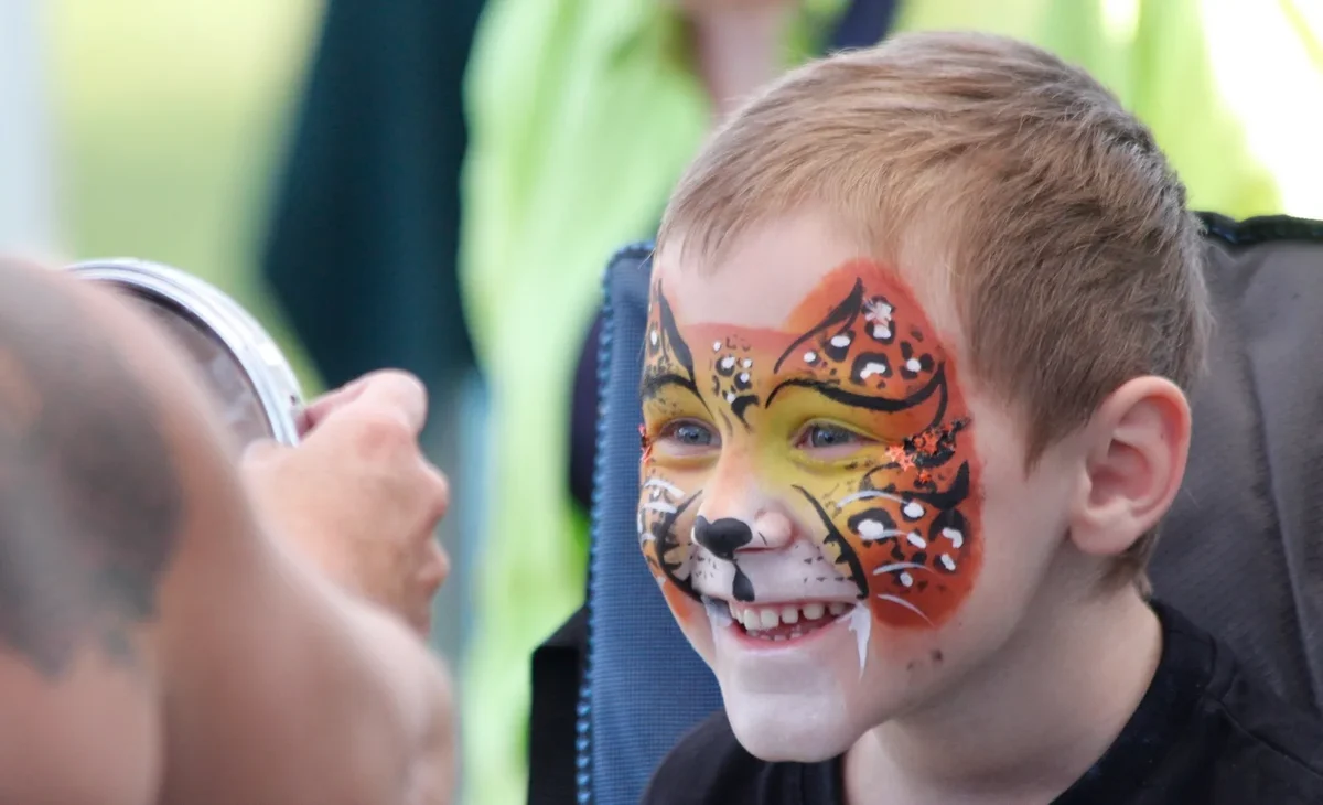 Boy grinning at his leopard face paint in Kat’s mirror