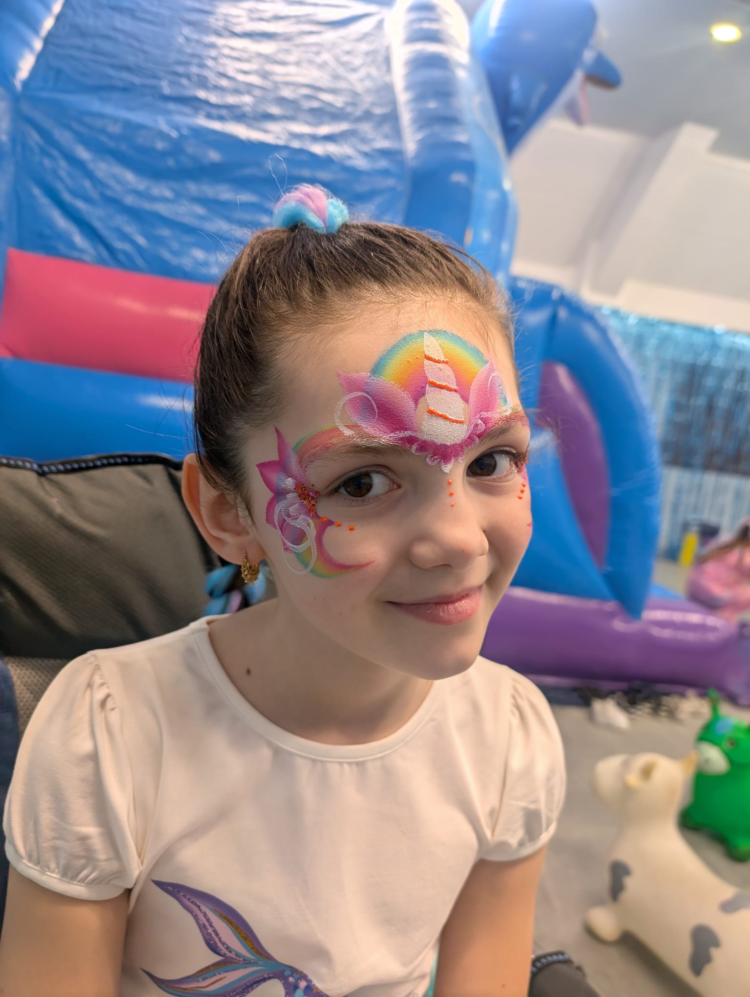 Unicorn rainbow face paint with pink sparkle horn for a girl